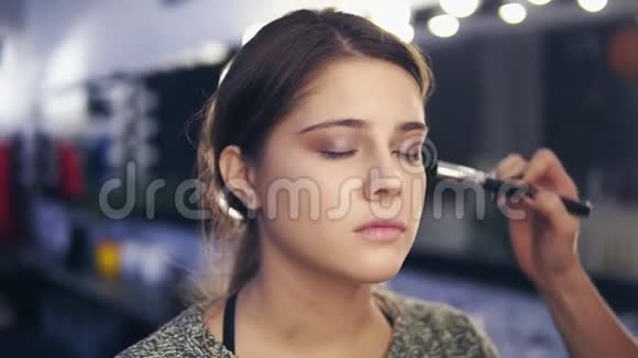 专业化妆师双手用专用刷子将面部粉涂于年轻女性皮肤特写镜头视频的预览图