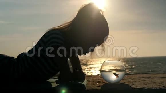 躺在海边的小女孩看着鱼缸里放着一条小鱼夏天在水面上倒影视频的预览图