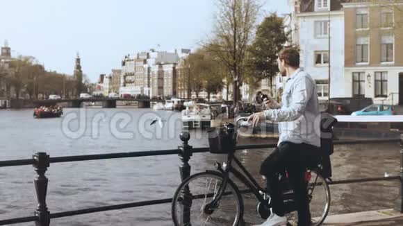 4K欧洲男子骑自行车在河桥上休闲时尚的男性类型的智能手机并环顾四周欣赏风景视频的预览图