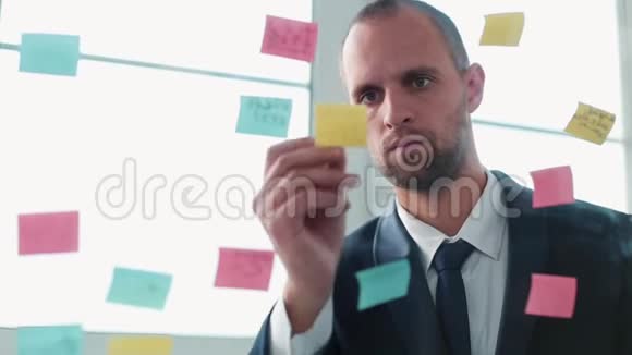 一个年轻人站在办公室里靠近一个有贴纸的透明板视频的预览图