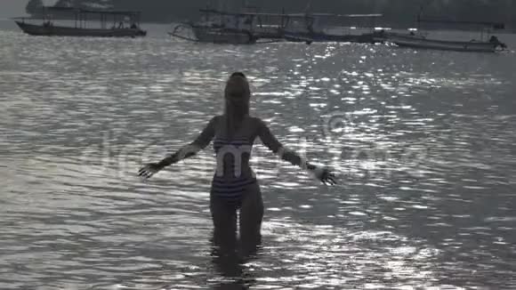 这位年轻苗条的幸福女人的轮廓她站在海里溅起双手视频的预览图