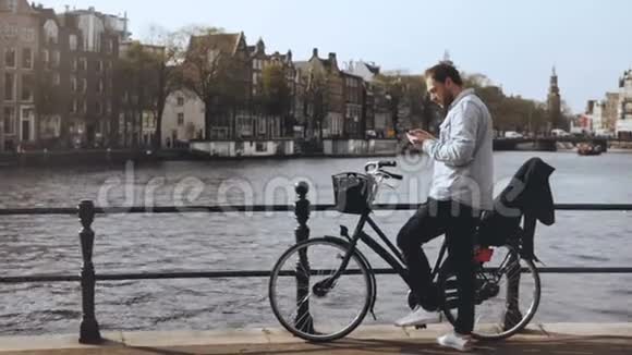带着手机在河桥上骑自行车的4休闲英俊的欧洲胡须男型一个信息和走开视频的预览图
