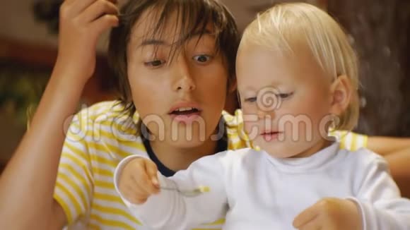 婴儿在餐馆吃食物快乐的蓝眼睛孩子用勺子喂养哥哥视频的预览图