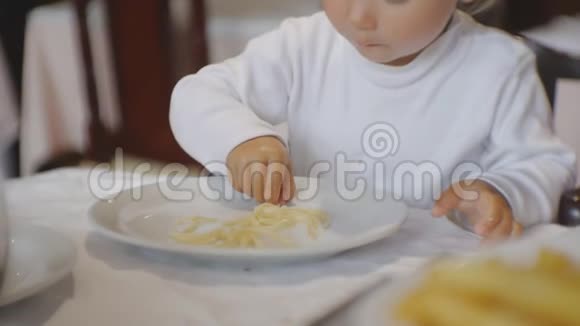 婴儿在餐馆吃食物坐在高椅上的金发碧眼的孩子用手拿着盘子里的意大利面视频的预览图