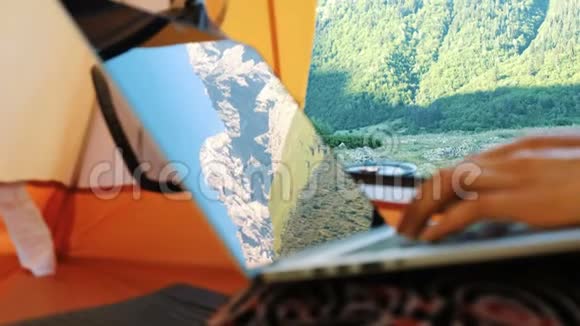 山脉反映在笔记本电脑屏幕上自由职业者在旅游帐篷使用电脑视频的预览图