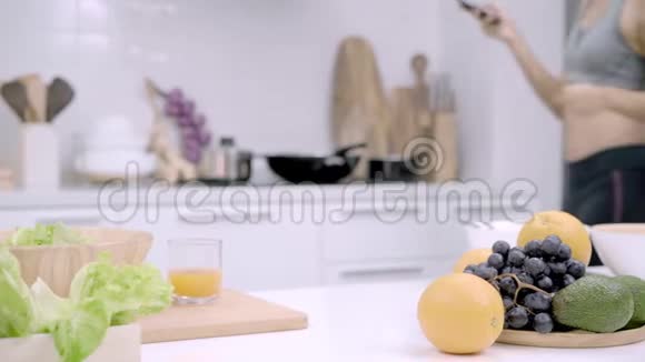 年轻的亚洲女人在厨房里喝橙汁做沙拉漂亮的女性在运动服装中使用有机水果视频的预览图