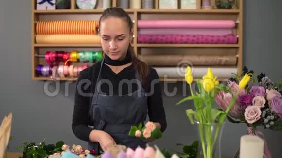 年轻的女性花店在花店里布置现代花束她结合了奶油玫瑰和黄色郁金香慢动作视频的预览图