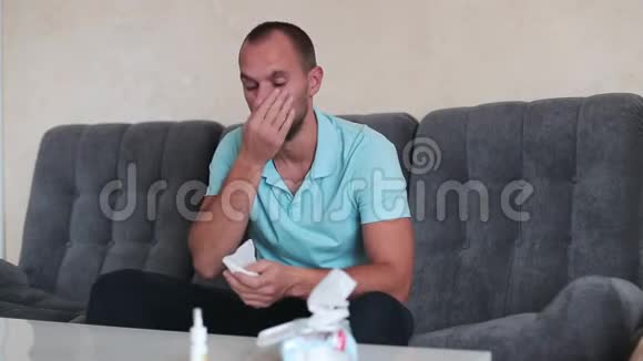 严重过敏沮丧的英俊青年坐在家里的沙发上打喷嚏和使用纸巾视频的预览图