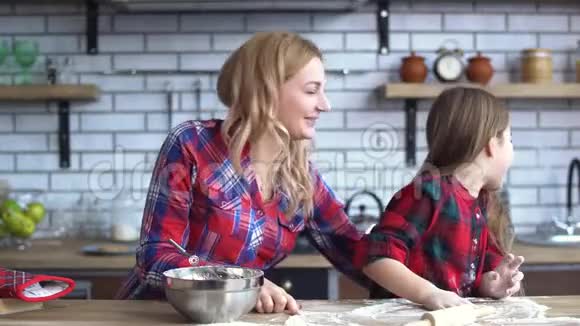 无忧无虑的年轻母亲和女儿在厨房的餐桌上做菜妈妈和孩子一起玩得很开心视频的预览图
