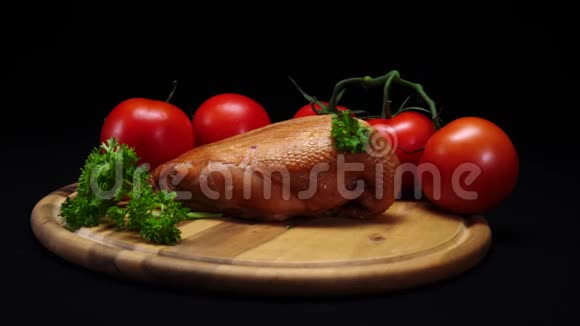 黑色背景的木板上躺着烤鸡西红柿和青菜的特写镜头框架视频的预览图