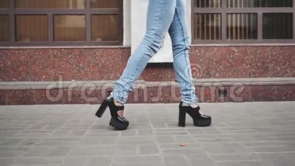 女人的腿穿着黑色的平台鞋和蓝色的牛仔裤走在城市的街道上视频的预览图