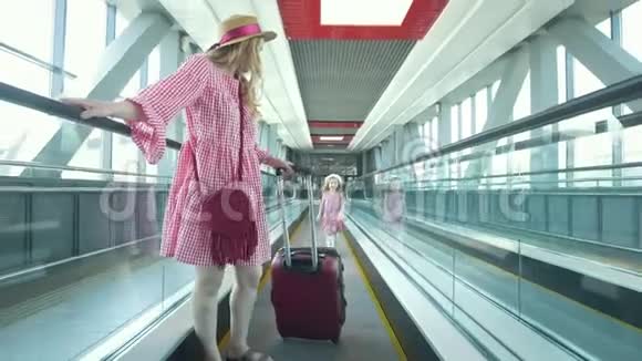 年轻漂亮的女人带着手提箱从扶梯上下来她漂亮的女儿在门口追赶她的母亲视频的预览图