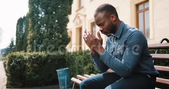 悲伤和沮丧的年轻黑人非洲商人坐在街道上的电话后疲惫坏消息的概念视频的预览图
