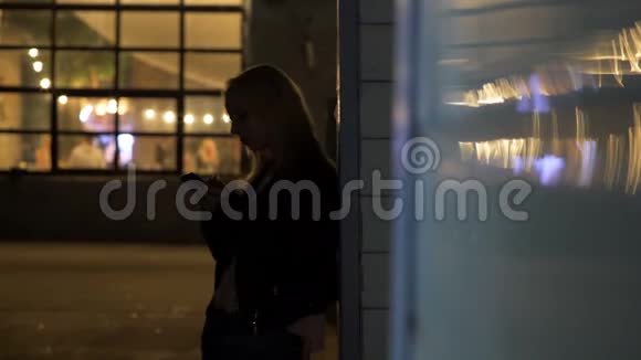 孤独的金发女人站在迪斯科厅附近在智能手机上打字视频的预览图