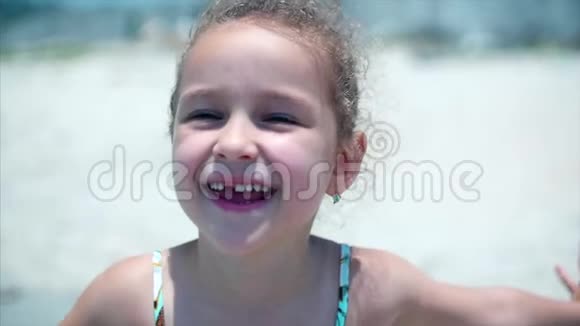 一个穿着泳装的迷人小女孩的肖像一个孩子微笑着站在沙滩上看着摄像机视频的预览图