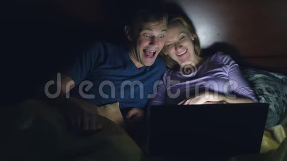 夫妻男人和女人在睡觉前在卧室的床上用笔记本电脑看电影看喜剧电影视频的预览图