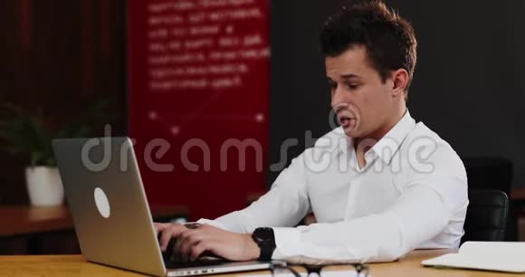 厌倦了在笔记本电脑上工作的年轻商人穿着白色衬衫揉了揉眼睛深呼吸工作狂视频的预览图
