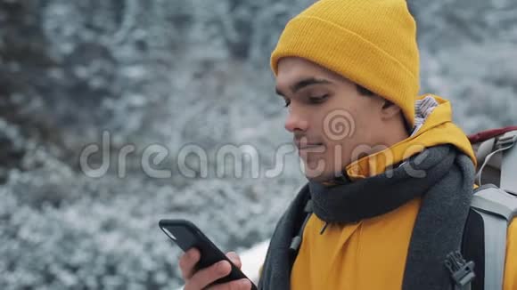 一位年轻的游客站在雪山上的一座桥上手里拿着一部智能手机徒步旅行者和视频的预览图