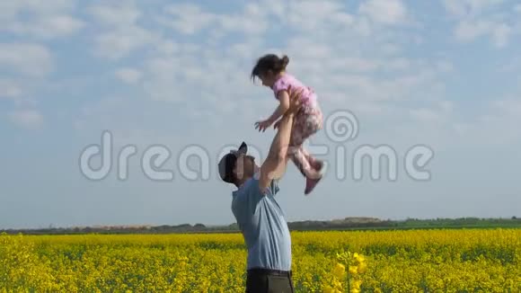 那个人把孩子扔了那个人把孩子扔了起来爸爸和女儿在大自然中玩耍在一片黄色的草地上幸福的家庭视频的预览图