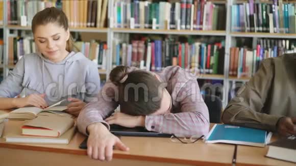 潘老师勤奋的学生准备考试做作业疲惫的家伙睡在大学图书馆的桌子上视频的预览图
