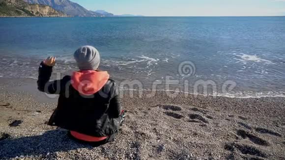 坐在海滩上的女孩的后景在水里扔石头的女孩视频的预览图