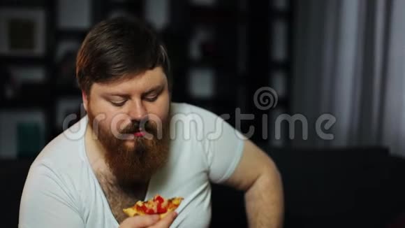 意志薄弱的超重男人坐在沙发上吃披萨喝啤酒营养不良体育运动肥胖的概念视频的预览图