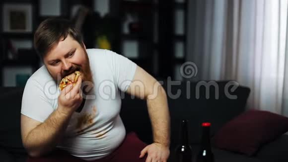 意志薄弱的超重男人坐在沙发上吃披萨喝啤酒营养不良体育运动肥胖的概念视频的预览图