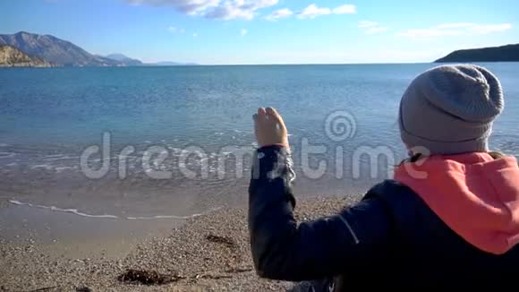 坐在海滩上的女孩的后景在水里扔石头的女孩视频的预览图