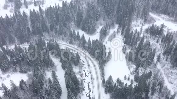 在冬季森林环绕的道路上行驶的汽车的鸟瞰图视频的预览图