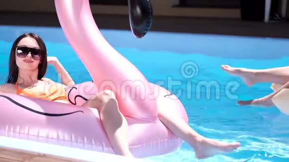 两个穿着五颜六色身材优美的泳装的快乐女孩正在游泳池里玩充气玩具视频的预览图