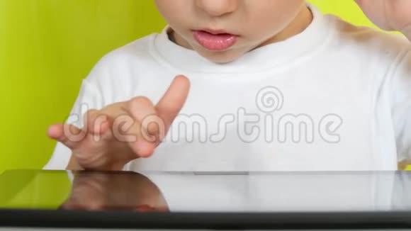 一个坐在桌子旁的孩子用手指触摸平板电脑的电子显示器特写镜头视频的预览图