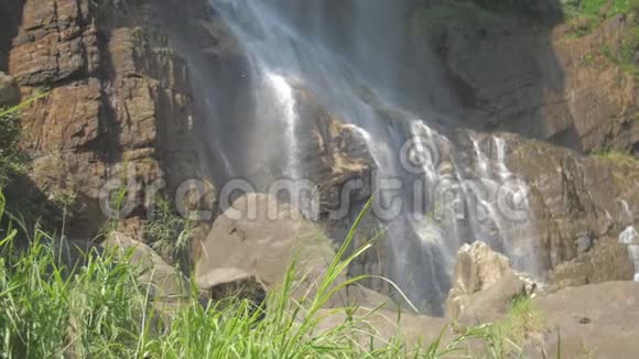 新鲜的水从高高的棕色岩石悬崖落下阳光照射视频的预览图