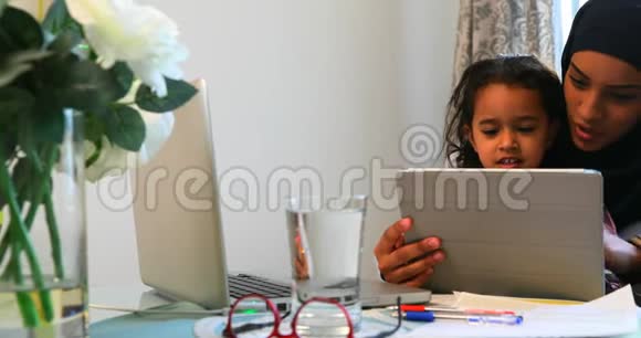 年轻的母亲用数字平板电脑她的女儿在桌子上4k视频的预览图