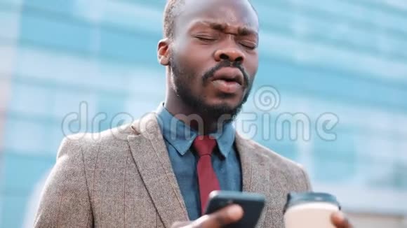 疲惫而紧张的非裔美国商人站在外面看着他的智能手机里的东西人短信发短信视频的预览图