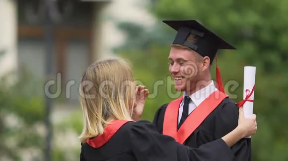 漂亮的年轻女人温柔地吻着男朋友快乐的一对毕业生视频的预览图