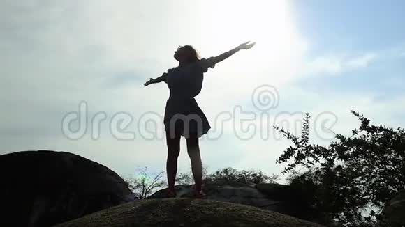 站在岩石上的年轻快乐的女人的剪影举起双手对着天空慢动作1920x1080视频的预览图