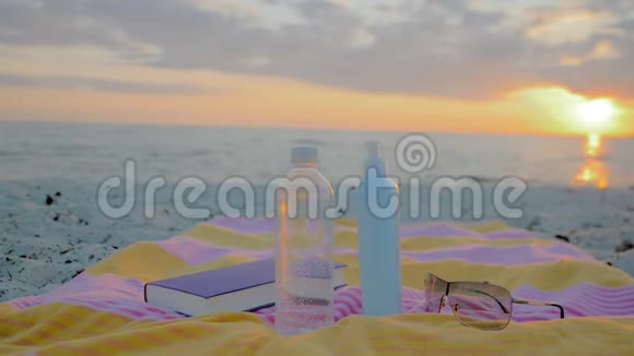 海滩用品一瓶水毛巾太阳镜防晒霜和一本书视频的预览图
