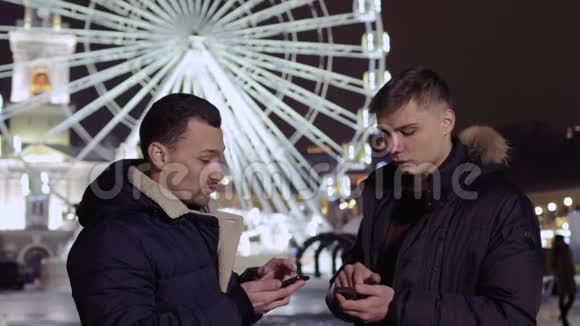 两个年轻人在摩天轮背景下使用手机视频的预览图
