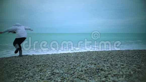 年轻女子在沙滩上散步怕在海水中弄湿鞋子溅起浪花视频的预览图
