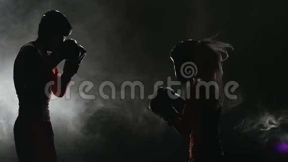 女孩在用拳击踢一个男人烟雾背景剪影慢动作视频的预览图