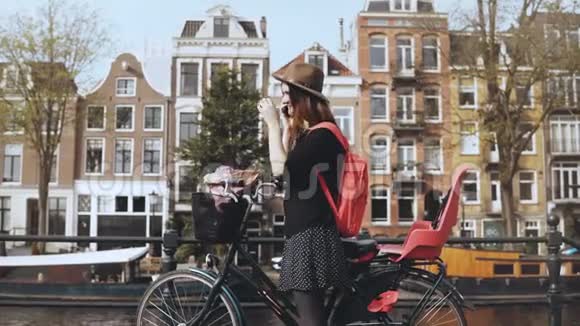微笑的女士在电话里交谈骑自行车离开年轻的女商人在一座宏伟的桥上荷兰阿姆斯特丹4K视频的预览图