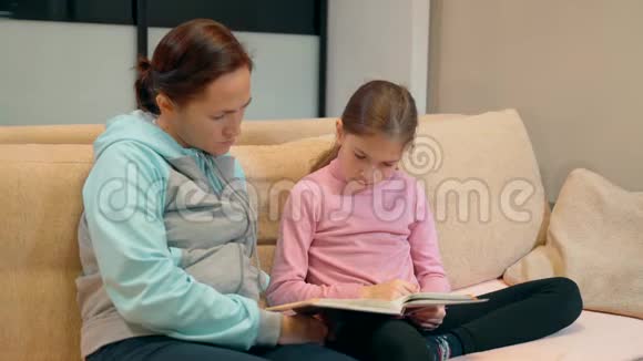 妈妈带着小女儿玩得很开心在家里的沙发上一起读这本书10岁的女孩和她妈妈视频的预览图