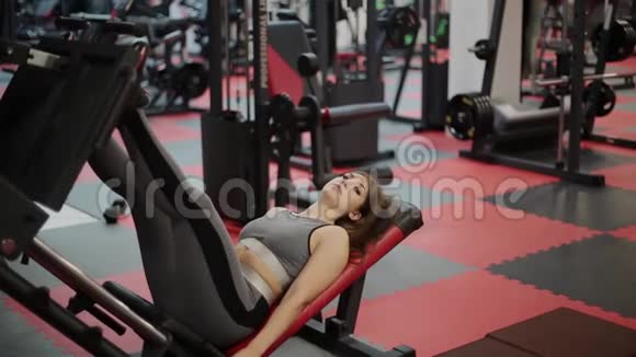 非常漂亮的健身女人在健身房的模拟器上训练她的腿视频的预览图