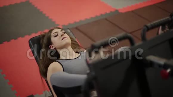 非常漂亮的健身女人在健身房的模拟器上训练她的腿视频的预览图
