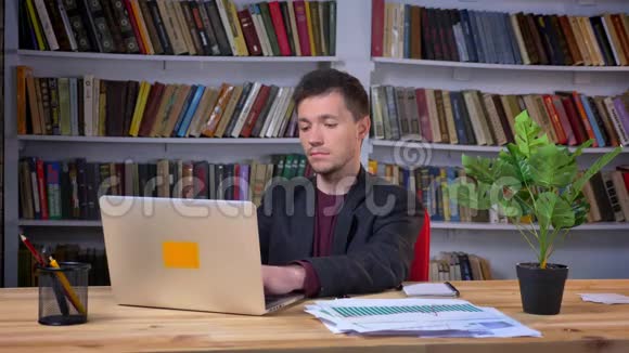 有魅力的成年男性在后台坐在图书馆的笔记本电脑上视频的预览图