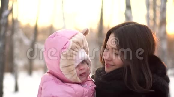在冬季公园的背景下在外面的雪树下特写婴儿和她年轻美丽的母亲的肖像快乐的母亲视频的预览图