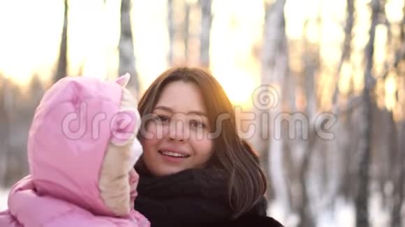 在冬季公园的背景下在外面的雪树下特写婴儿和她年轻美丽的母亲的肖像快乐的母亲视频的预览图