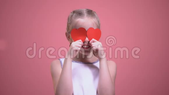 有趣的小女孩闭上眼睛红色的纸心被隔离在粉红色的背景上视频的预览图