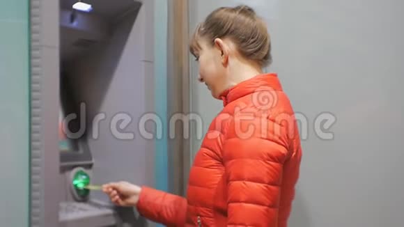 女人用提款机漂亮的年轻女性穿着红色泡沫夹克在ATM机上插入信用卡女人微笑视频的预览图