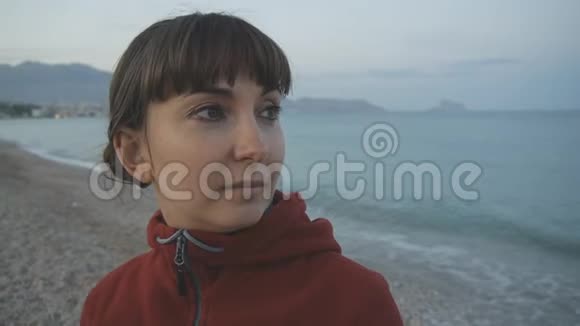 空滩背景的年轻女子穿着红色连帽衫的白种人棕色头发的迷人女性的特写镜头视频的预览图